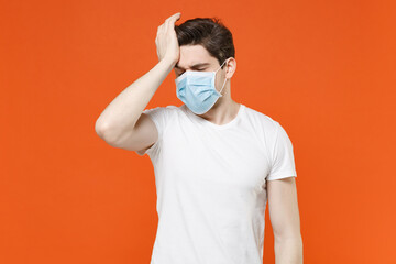 Wall Mural - Sick young man 20s in white t-shirt sterile face mask to safe from coronavirus virus covid-19 during pandemic quarantine having headache put hand on head isolated on orange background studio portrait.