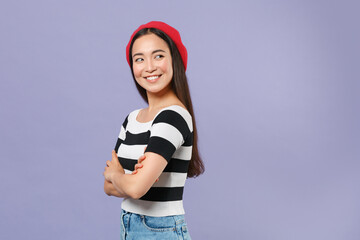 Wall Mural - Side view of smiling cheerful pretty young brunette asian woman in striped t-shirt red beret standing holding hands crossed looking aside isolated on pastel violet colour background studio portrait.