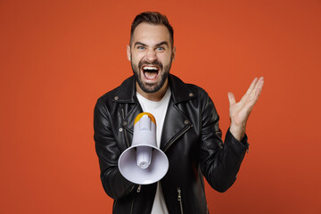 Wall Mural - Crazy shocked young bearded man wearing casual basic white t-shirt, black leather jacket standing screaming in megaphone spreading hands isolated on bright orange colour background studio portrait.