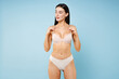 © ViDi Studio - Stunning gorgeous pretty thin young brunette woman 20s in beige underwear showing sports body standing posing hold hands on chest looking aside isolated on pastel blue background, studio portrait.