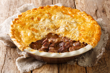 English homemade ale beef steak pie with crispy puff pastry close-up in a baking dish on the table. horizontal