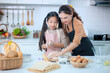 © pornchai - Happy Asian mother and adorable daughter helping knead the dough to make a bakery in the kitchen.