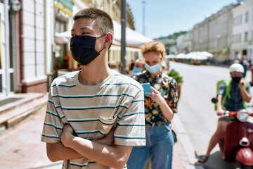 Wall Mural - Young asian guy wearing mask waiting in line, respecting social distancing to enter takeout restaurant or to collect purchases from the pickup point during coronavirus lockdown