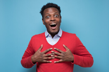 Canvas Print - Astonished afro american guy being surprised receiving compliment. Studio shot on blue wall.