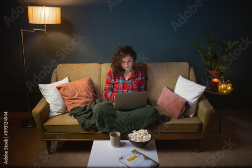 Cuadros en Lienzo A young modern woman with a laptop late at night sits on the couch and surfs the Internet, makes purchases, watches a video, writes