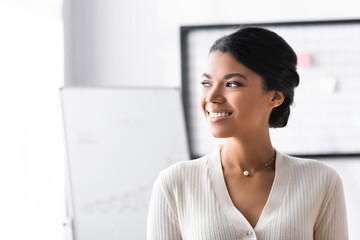 Wall Mural - Happy african american woman looking away while standing in office on blurred background