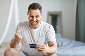 Poster - Joyful Man Holding Smartphone Credit Card Gesturing Yes At Home