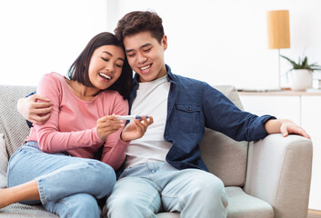 Wall Mural - Chinese Couple Holding Positive Pregnancy Test Sitting At Home