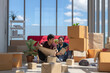 © Nutnutchar - Young Asian couple relax together after moving house. Lean against red sofa with many boxes in living room. Talking or discuss with house plan and design.