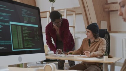 Panning of young Caucasian man and African-American man discussing new design project while young Caucasian female program developer sitting at workplace and coding on computer