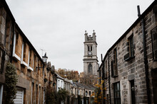 Perspective View Of Old Narrow Street With Grunge Residential Buildings On Background Of Gray Sky In Scottish Highlands