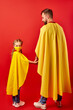 © Roman - father and daughter ready to fight against coronavirus, they stand in superhero costume, girl in medical mask, look at camera. isolated over red background