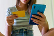 © David Munoz/ADDICTIVE STOCK - From below of unrecognizable crop female sitting at home and making payment with plastic card via cellphone while shopping online