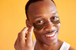 © Roman - excited afro american man with under eye patches smiling at camera isolated over yellow background, he gets anti aging beauty procedures