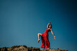 © Lucia Romero/ADDICTIVE STOCK - From below low angle side view of barefoot female in long red dress moving gracefully and balancing on leg on rough hill
