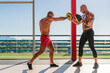 © Javier De La Torre/ADDICTIVE STOCK - Side view of strong male boxer doing punches in boxing mitts put on trainer in spacious gym during workout