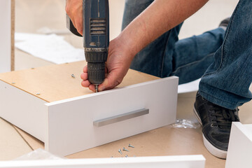 Wall Mural - Assembly of furniture, the carpenter screws a self-tapping screw into a drawer with a screwdriver