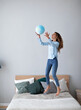 © BestForYou - Young happy woman jumping on the bed and tossing up the globe. Have fun at home.