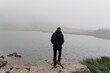 © Rabizo Anatolii - Men tourist is travelling and standing on the rocks near foggy lake. Hiking and climbing up to the top of the mountain. Tourism in Ukraine.