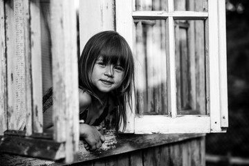 Little cute girl looks out the window country house. Black and white photo.