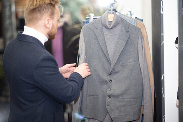 blonde millennial man in a business attire chooses clothes in a store. The man is shopping.