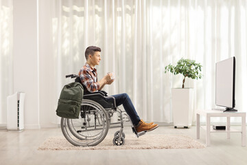 Canvas Print - Young man in a wheelchair with a cup of tea watching tv