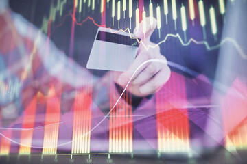 Double exposure of man hands holding a credit card and Forex graph drawing. Stock trading and digital fintech in Internet E-commerce concept.