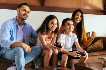 Wall Mural - Latin family enjoying the day together at home playing video games on the couch