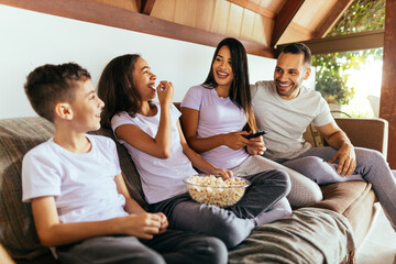 Wall Mural - Latin family enjoying the day together at home watching tv on the couch wearing pajamas