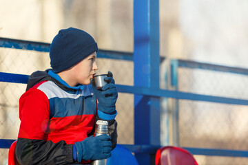 Wall Mural - A boy in soccer sportswear drinks hot water from a thermos bottle. Young footballer after the game. Training, active lifestyle, sport, children winter activity