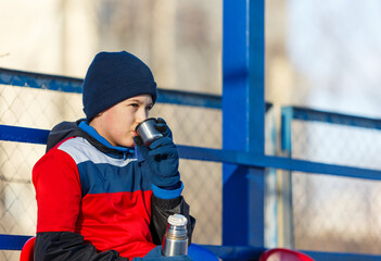 Wall Mural - Boy in soccer sportswear drinks hot water from thermos bottle . Young footballer after game. Training, active lifestyle, sport, children winter activity