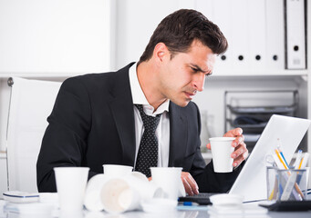 Tired man with loosened tie and disposable cup working in hot office