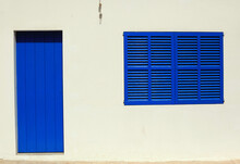 Blue Wooden Door And A Window On A Bright White Wall In Ibiza, Spain