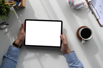Fototapete - Top view of man sitting at work space and using tablet with white screen for advertising text.