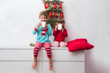 Two kids brother and sister in pajamas drinking cocoa with sweets from advent calendar at home. Hygge. Happy family on Christmas holiday.