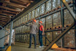 © zinkevych - Manager in orange helmet talking to a warehouse worker and showing him containers