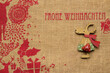 Frohe Weihnachten Rentier mit rotem Herz mit weissen Punkten und grünem Rock und rotem Schal aus Holz auf Hintergrund aus Jute mit rotem Druck      FROHE WEIHNACHTEN und skandinavischen Ornamenten 