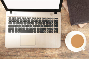 Laptop computer white blank screen with cup of coffee and notebook on work table. Flat lay.