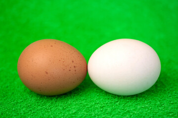 White and brown fresh eggs kissing each other isolated on green background macro