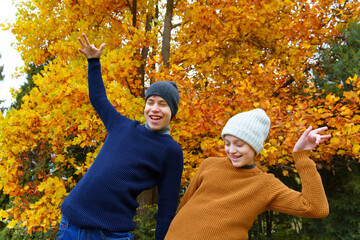 Wall Mural - teen girl and boy in autumn city park, posing and playing on a background of yellow maple leaves, beautiful nature