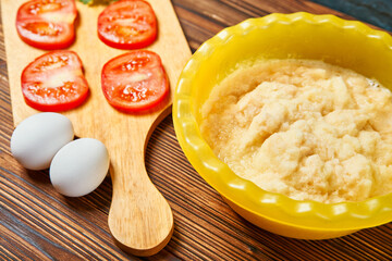 grated potato sliced red tomatoes two eggs on a wooden table. cooking potato pancakes