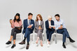 © LIGHTFIELD STUDIOS - Multiethnic businesspeople with coffee to go using devices on chairs on grey background