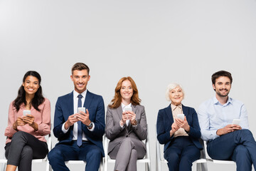 Wall Mural - Smiling multicultural businesspeople using smartphones isolated on grey