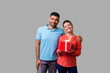 © khosrork - Portrait of satisfied young couple in casual wear hugging, delighted woman holding gift box, holiday present, looking at camera with toothy smile. isolated on gray background, indoor studio shot