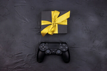 Joystick gaming controller and gift box with gold ribbon on black background. Holiday sale or black friday concept.