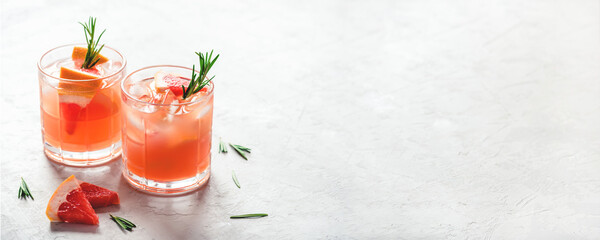 Wall Mural - Refreshing grapefruit cocktail with ice and rosemary on a grey background.