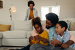 © bernardbodo - Afro parents and their children are socializing while sitting on the sofa
