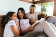 © kleberpicui - Latin family enjoying the day together at home. Family reading together on the couch in the morning.