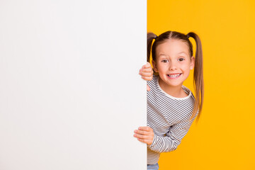 Canvas Print - Photo of young happy smiling little girl child kid stand behind white wall isolated on yellow color background