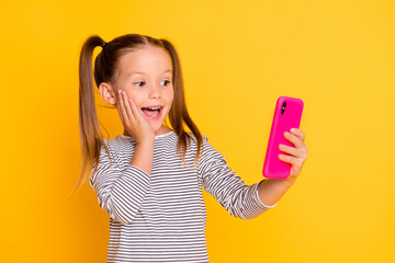 Sticker - Portrait of young surprised amazed little girl child kid hold cellphone smartphone isolated on yellow color background